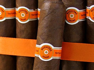 A single Tatuaje Nuevitas cigar resting on a dark wooden surface, showcasing its Corojo ’99 wrapper