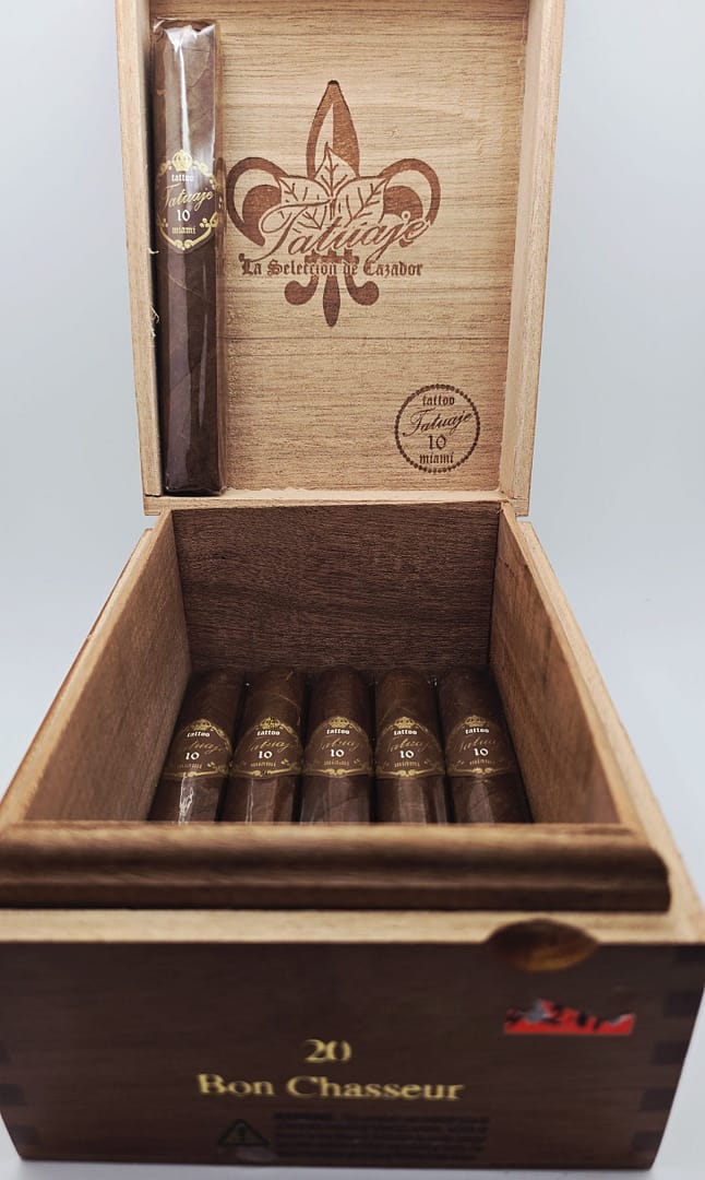 This image features a single Tatuaje 10th Anniversary cigar placed on a polished wooden surface. The cigar showcases a rich, dark wrapper with a slightly oily sheen and a box-pressed shape. The cigar’s distinct red-and-black anniversary band stands out, symbolizing the brand’s 10th year of fine craftsmanship. Known for its full-bodied profile and complex flavors, the Tatuaje 10th Anniversary is a must-have for aficionados seeking a rich, Nicaraguan experience.