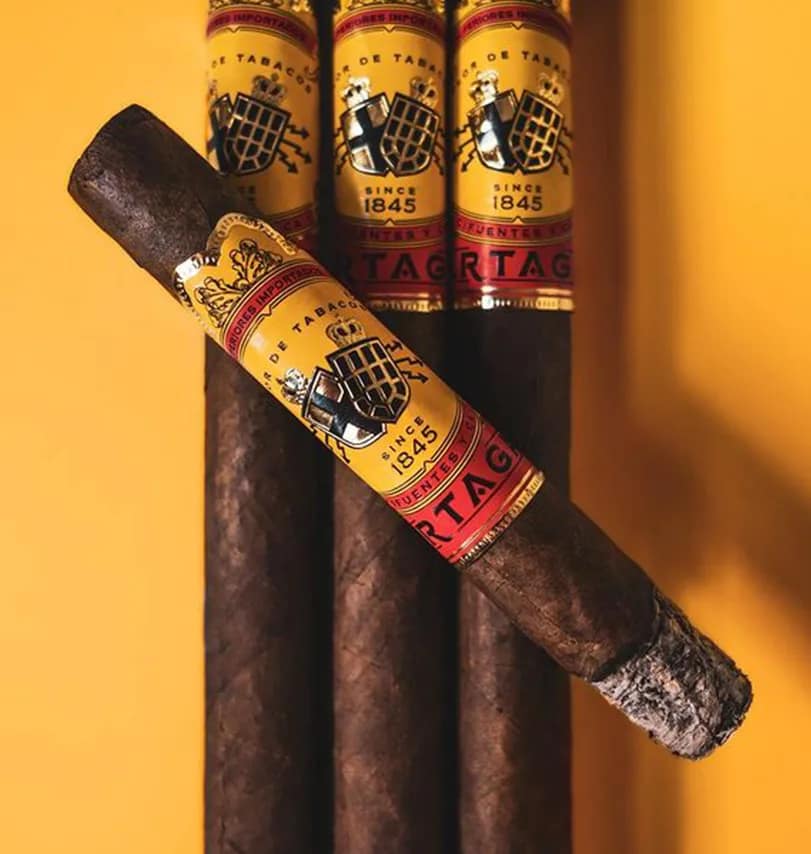 A lit Partagás Classic cigar resting on three unlit Partagás Classic cigars, with soft smoke rising.