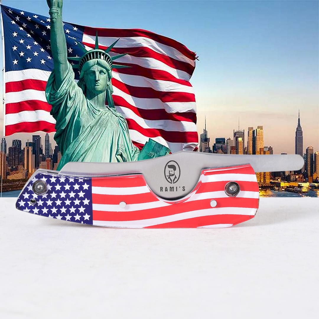 Rami’s American Flag Cigar Knife closed, placed in front of the Statue of Liberty and an American flag, highlighting the patriotic handle and sleek blade