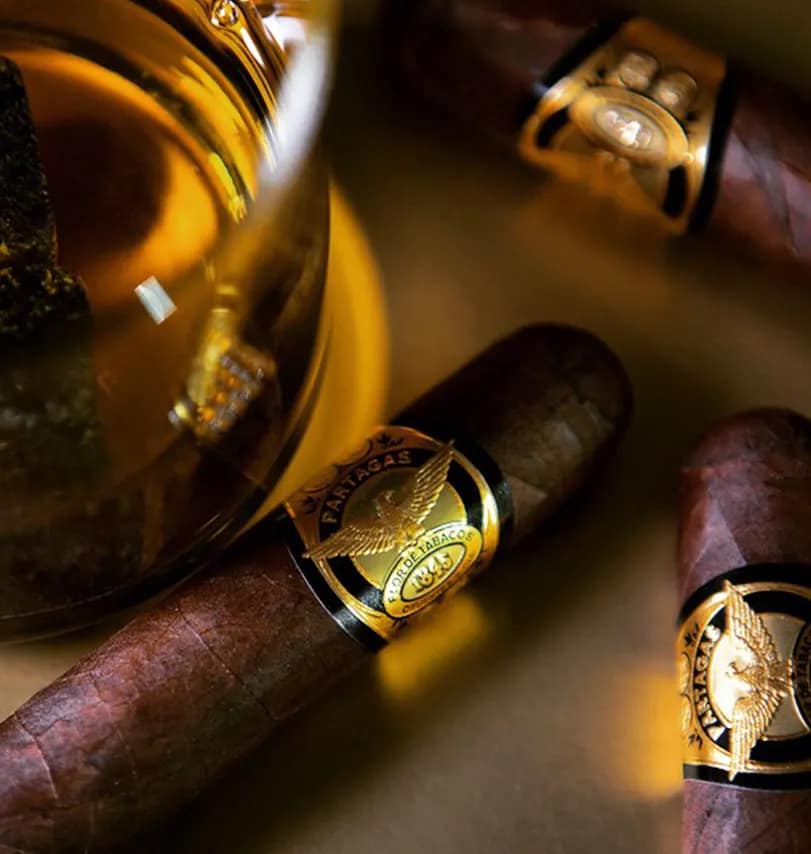 Three Partagás 1845 Clásico cigars arranged around a glass of cognac on a wooden surface.