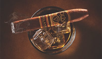 A lit Oliva Serie V Melanio cigar placed on a glass of cognac, highlighting a perfect blend of sophistication