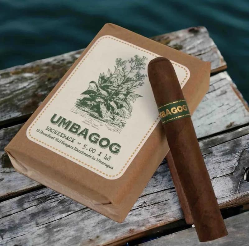 Single Umbagog cigar resting on a bundle of dark-wrapped cigars with rustic bands